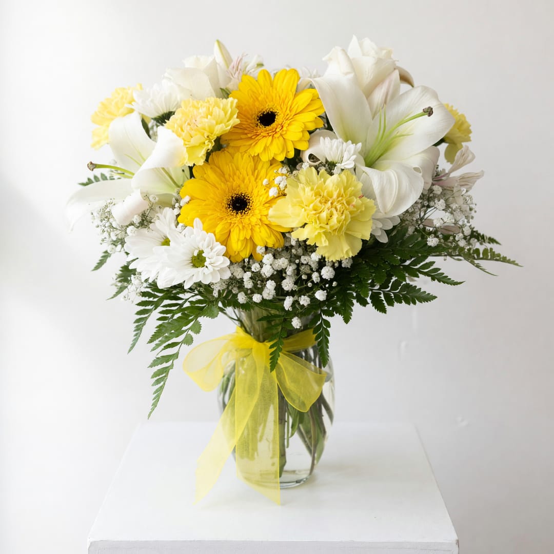 Yellow and white bouquet in a glass vase with a yellow ribbon