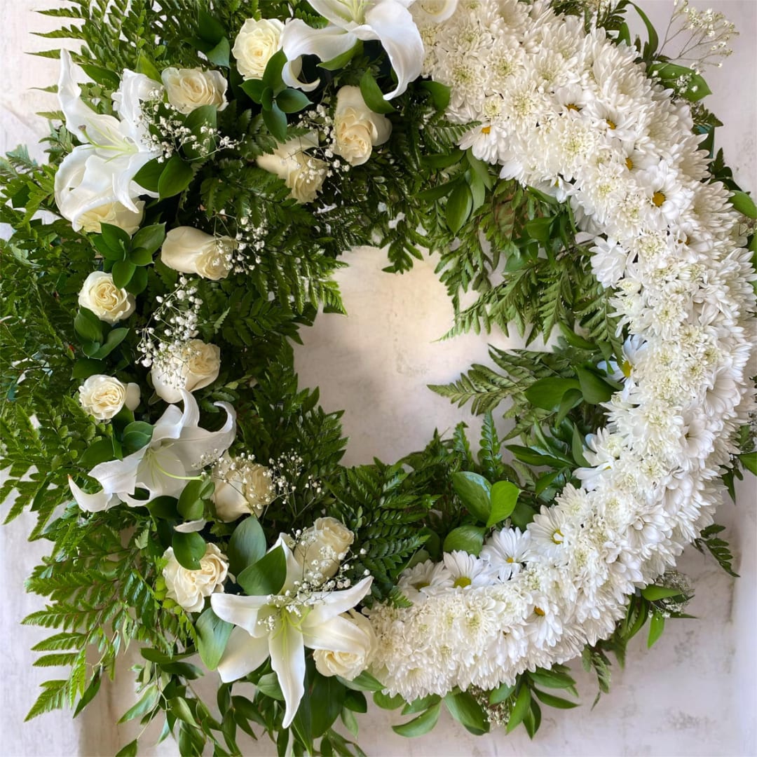 White floral wreath with lilies, roses, and daisies on a light background