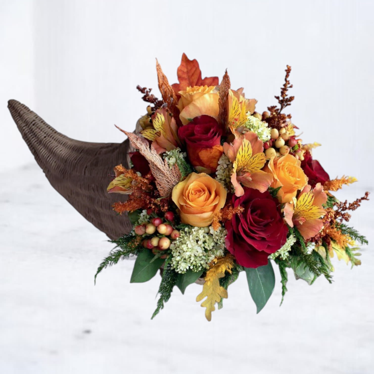 Gilded Abundance Cornucopia Centerpiece - Celebrate the beauty of gratitude with our Gilded Abundance Cornucopia Centerpiece, a radiant display of autumn’s finest blooms. Designed with glowing orange and golden roses, warm red alstroemeria, seasonal berries, and harvest textures, this arrangement captures the spirit of Thanksgiving in timeless style.  Nestled within a natural woven cornucopia, each bloom is artfully placed to create balance, depth, and movement — a perfect expression of abundance and appreciation. Ideal for Thanksgiving gatherings, fall dinner parties, or as a thoughtful hostess gift, this piece brings warmth and elegance to every table.  Perfect For: Thanksgiving tables, fall celebrations, and seasonal gifting.
