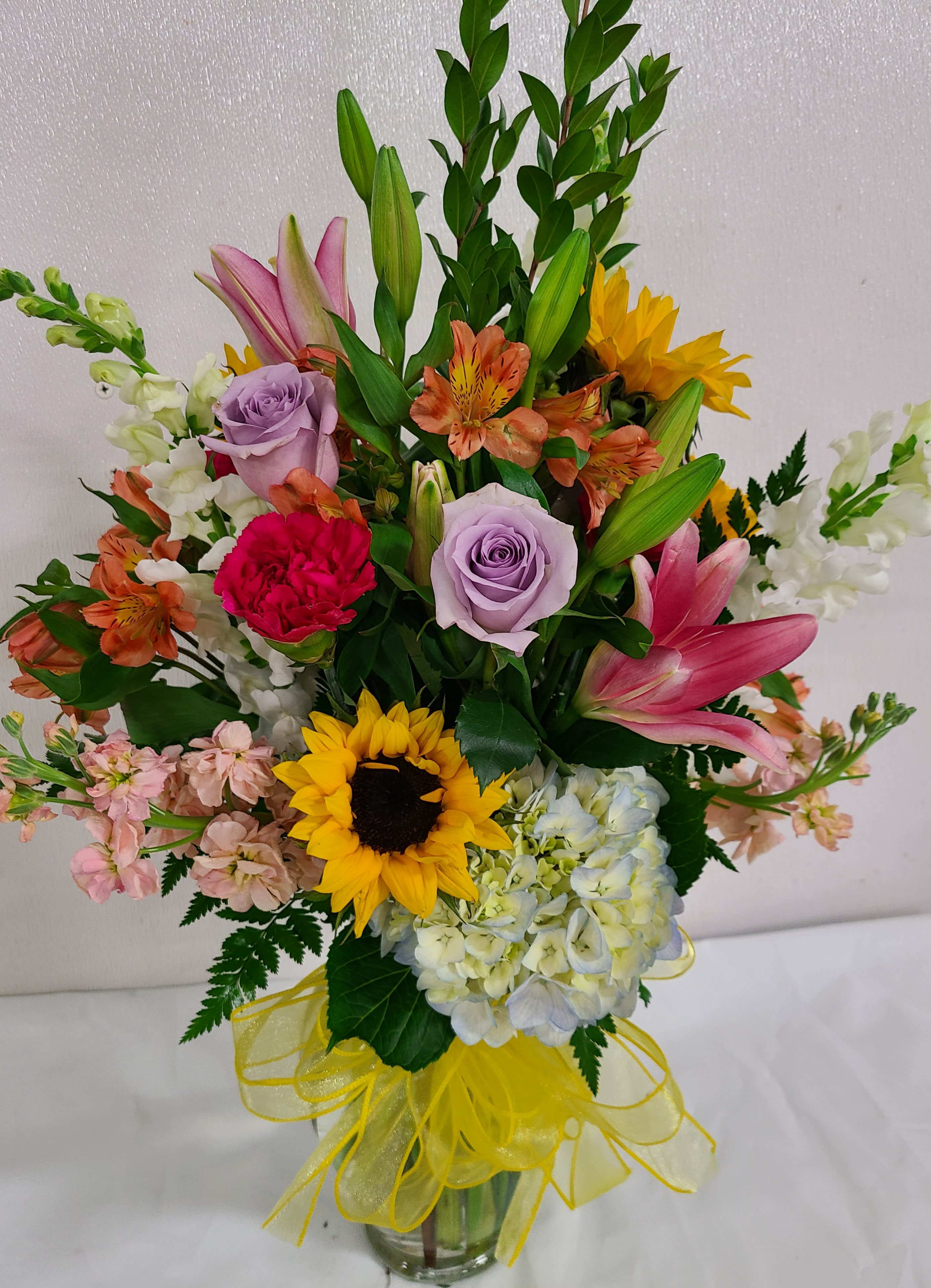 Mixed bouquet with sunflowers, lilies, roses, and hydrangeas in a glass vase