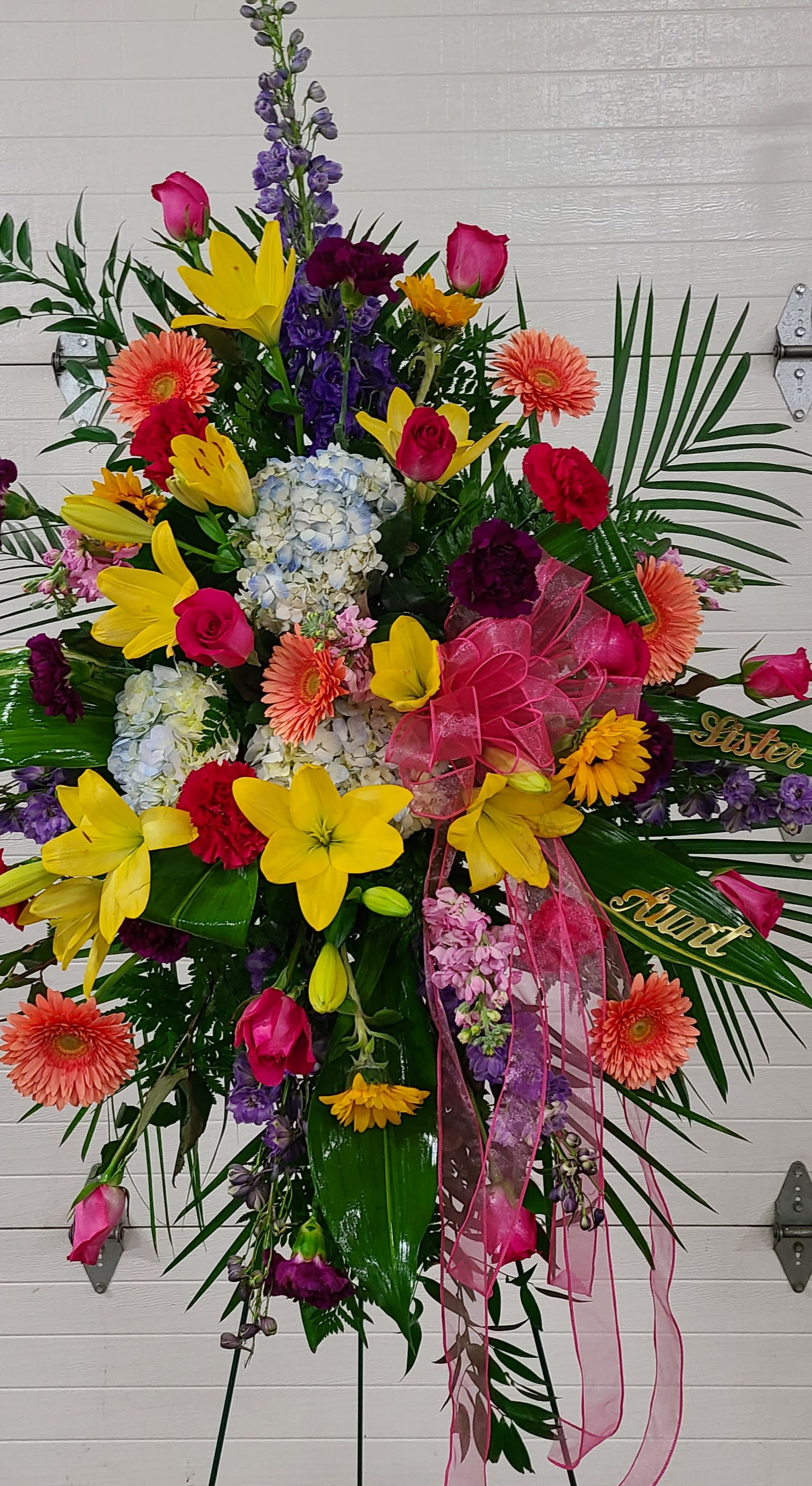 Large standing floral spray with bright mixed blooms and pink ribbon