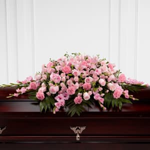 Pink floral casket spray on a dark wooden casket