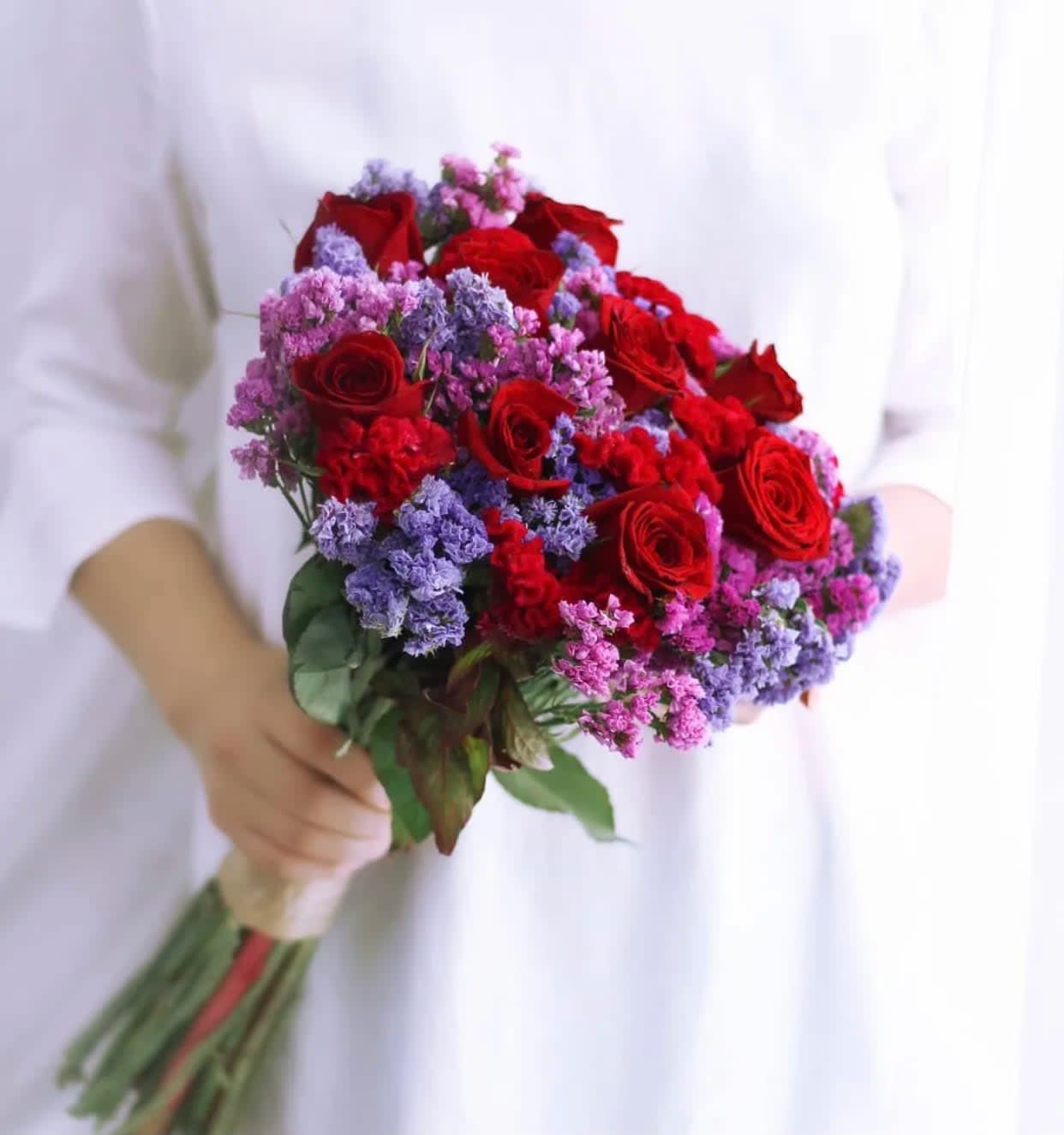 Handheld bouquet of red roses with purple and pink filler flowers
