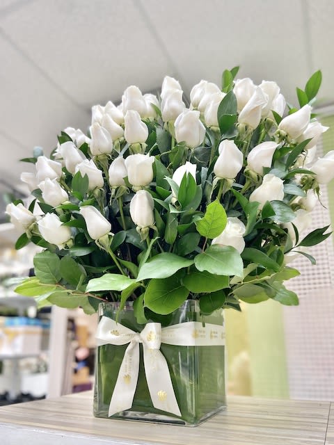 Arrangement of white rosebuds in a clear square vase with white ribbon
