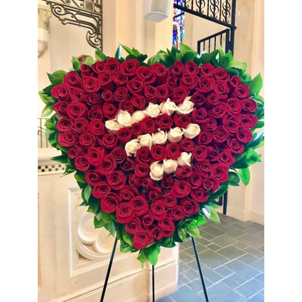 Large heart-shaped arrangement of red and white roses bordered with foliage on a black metal easel.