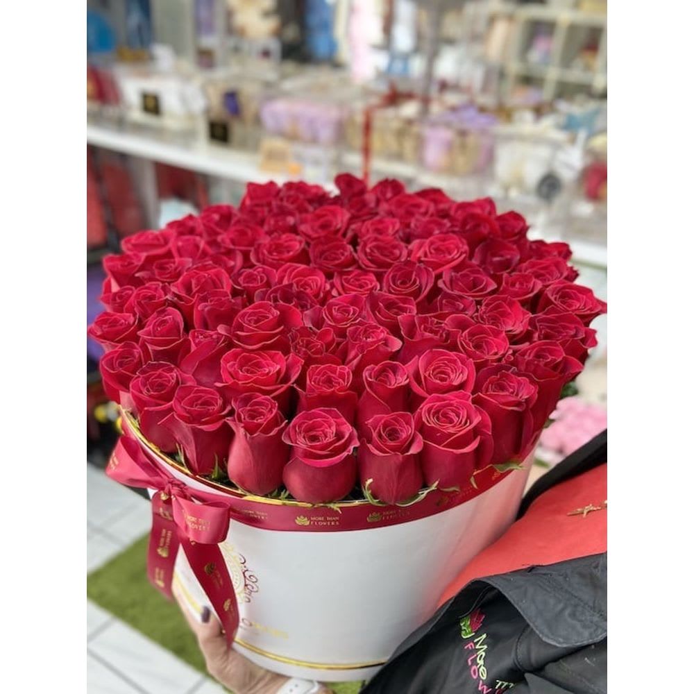 Large round box filled with tightly packed red roses and tied with a red ribbon