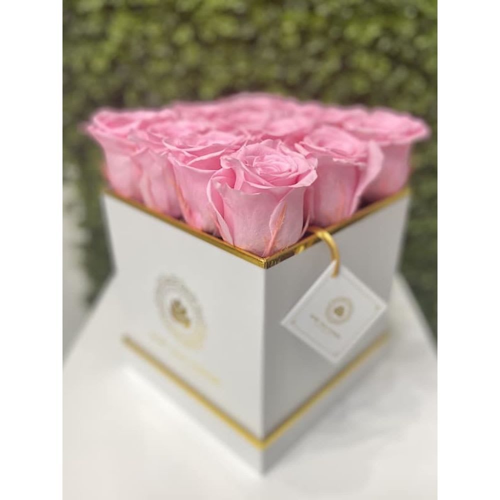 Square white box filled with tightly packed pink roses on a white surface