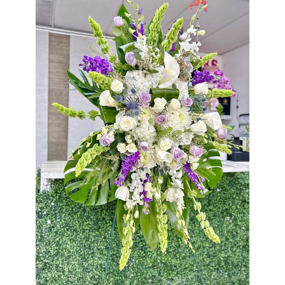 Tall standing spray of white and lavender flowers with bells of Ireland on a green easel