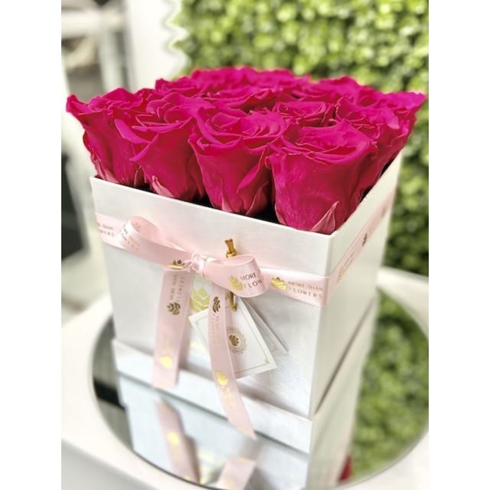 Square white box filled with bright fuchsia roses and tied with a pink ribbon