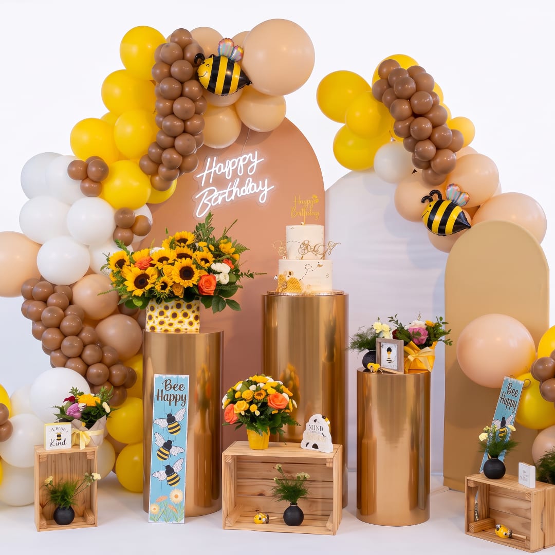 Birthday display with balloon arches, sunflowers, and a cake on gold pedestals