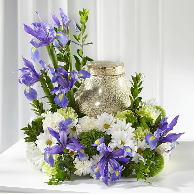 Purple irises and white daisies arranged around a decorative urn.