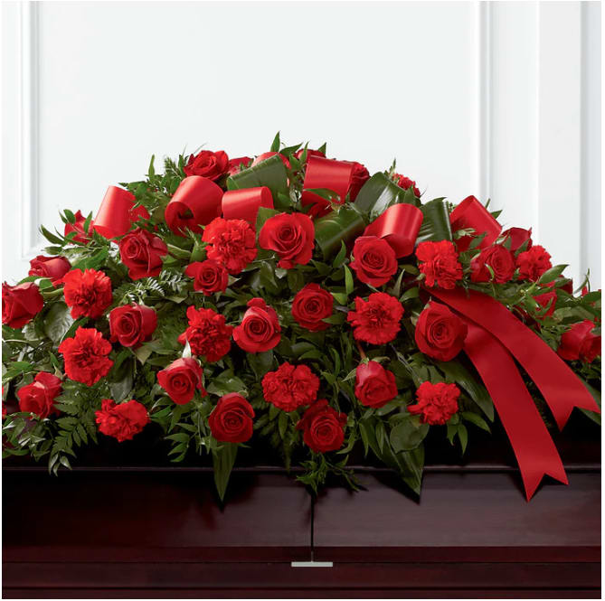 Red roses and carnations arranged on a casket with red ribbon