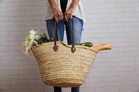 Person holding a large woven market basket with groceries and flowers