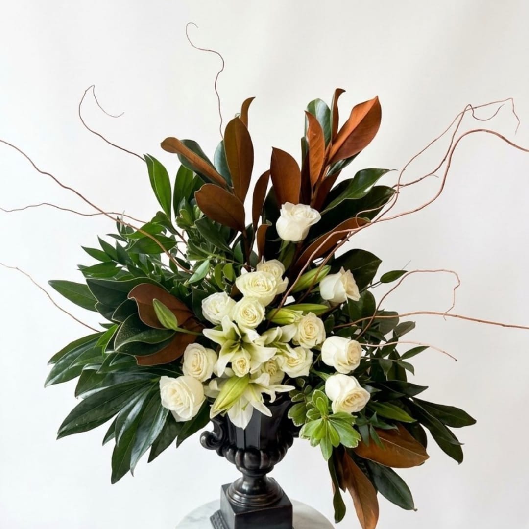 White roses and lilies in a black urn vase with branching twigs