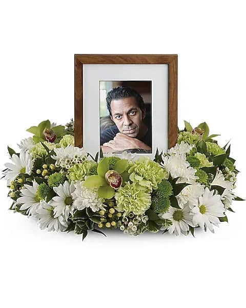 Framed photo surrounded by white and green funeral flowers