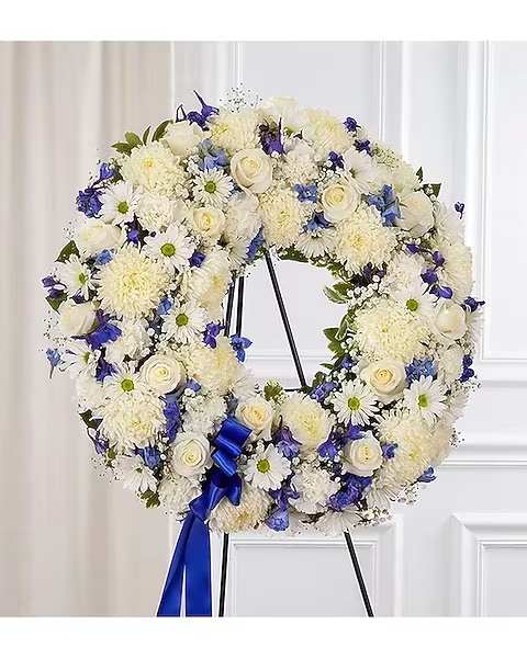White and blue floral wreath on a black stand with a blue ribbon