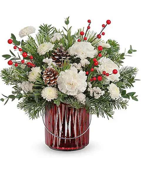 White flowers and pine arranged in a red glass vase with red berry accents