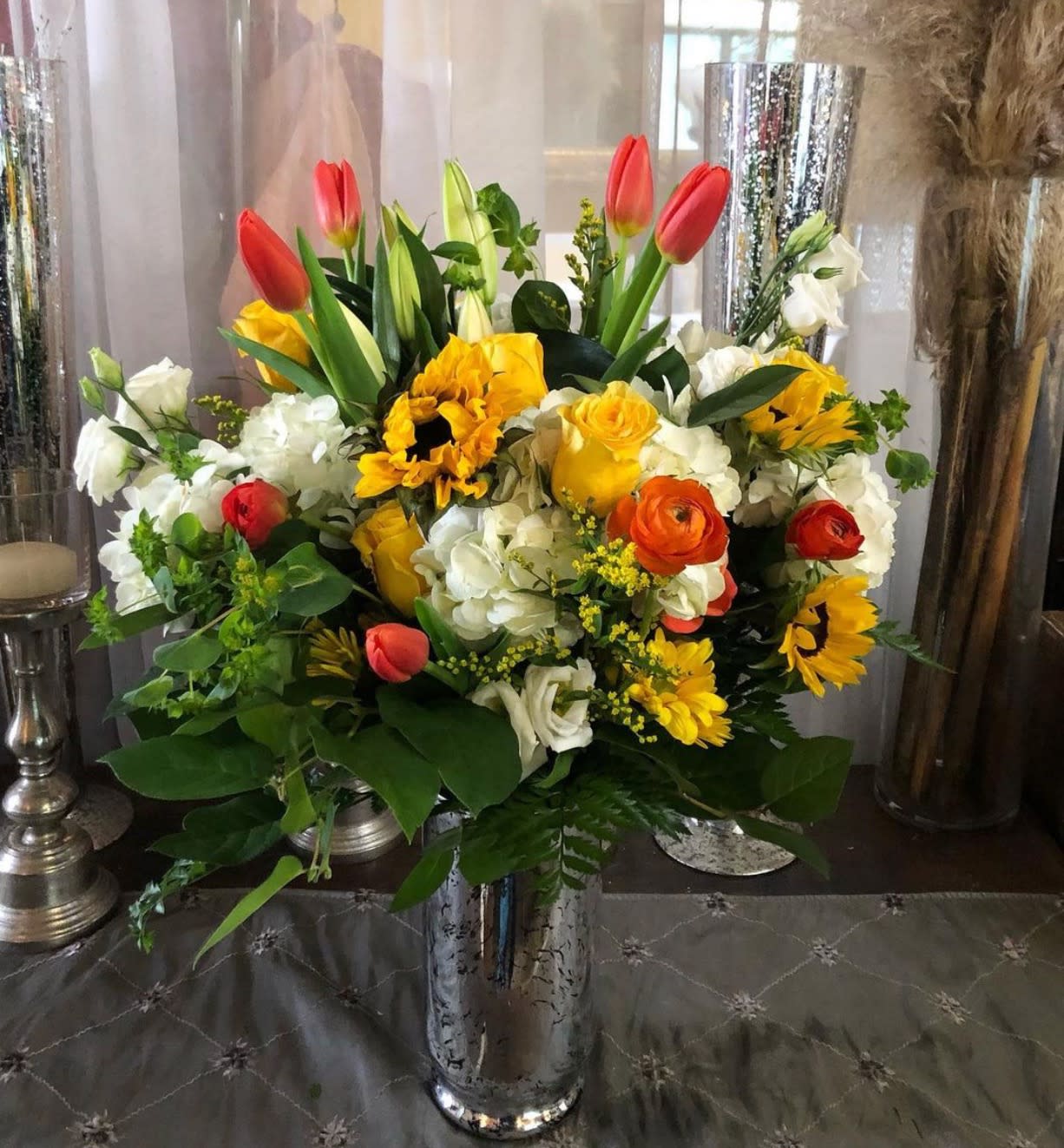 Mixed bouquet with tulips, roses, sunflowers, and white blooms in a silver vase