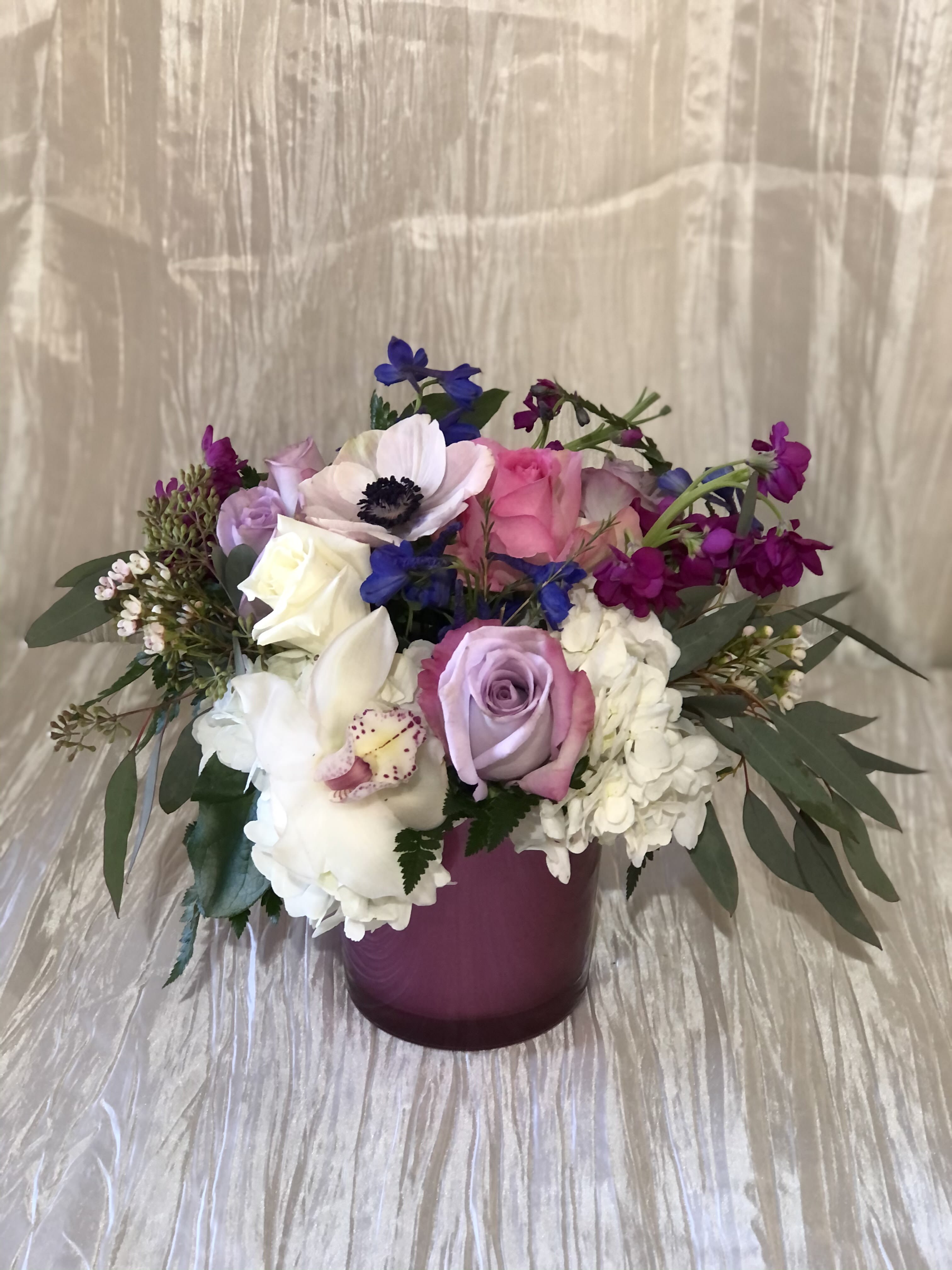 Mixed bouquet of roses, orchids, and hydrangeas in a purple vase