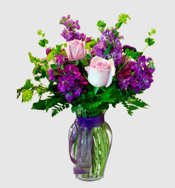 Pink roses and purple flowers arranged in a glass vase with a purple ribbon