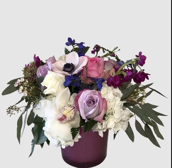 Mixed bouquet of roses, hydrangeas, and orchids in a purple vase