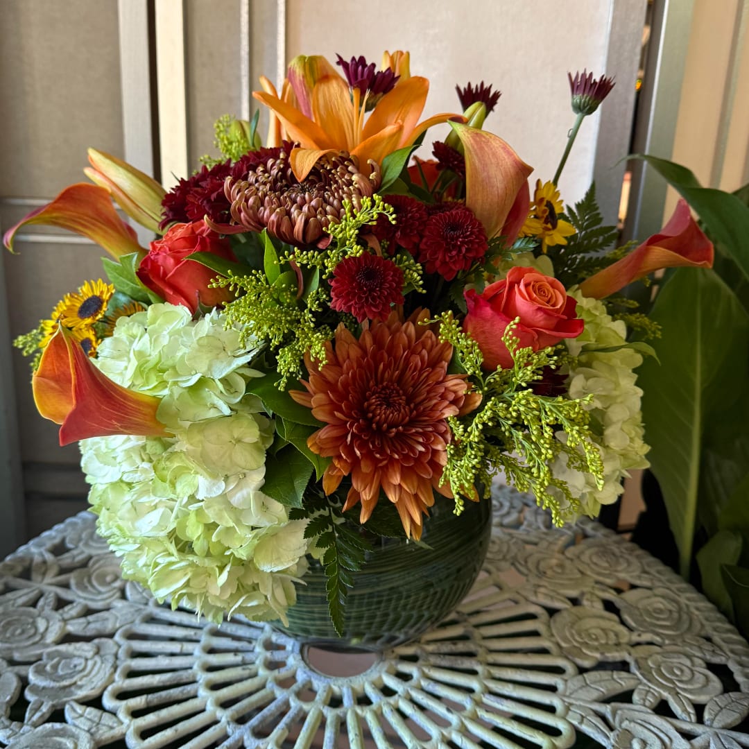 Mixed bouquet with orange lilies, roses, chrysanthemums, and pale hydrangeas in a green vase