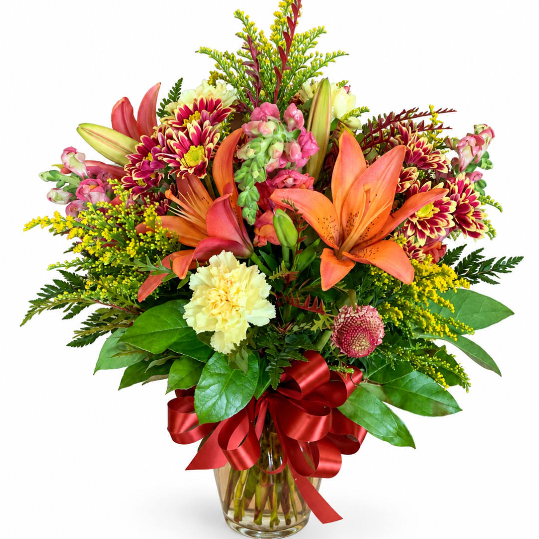 Mixed bouquet of lilies, chrysanthemums, and carnations in a glass vase with a red ribbon