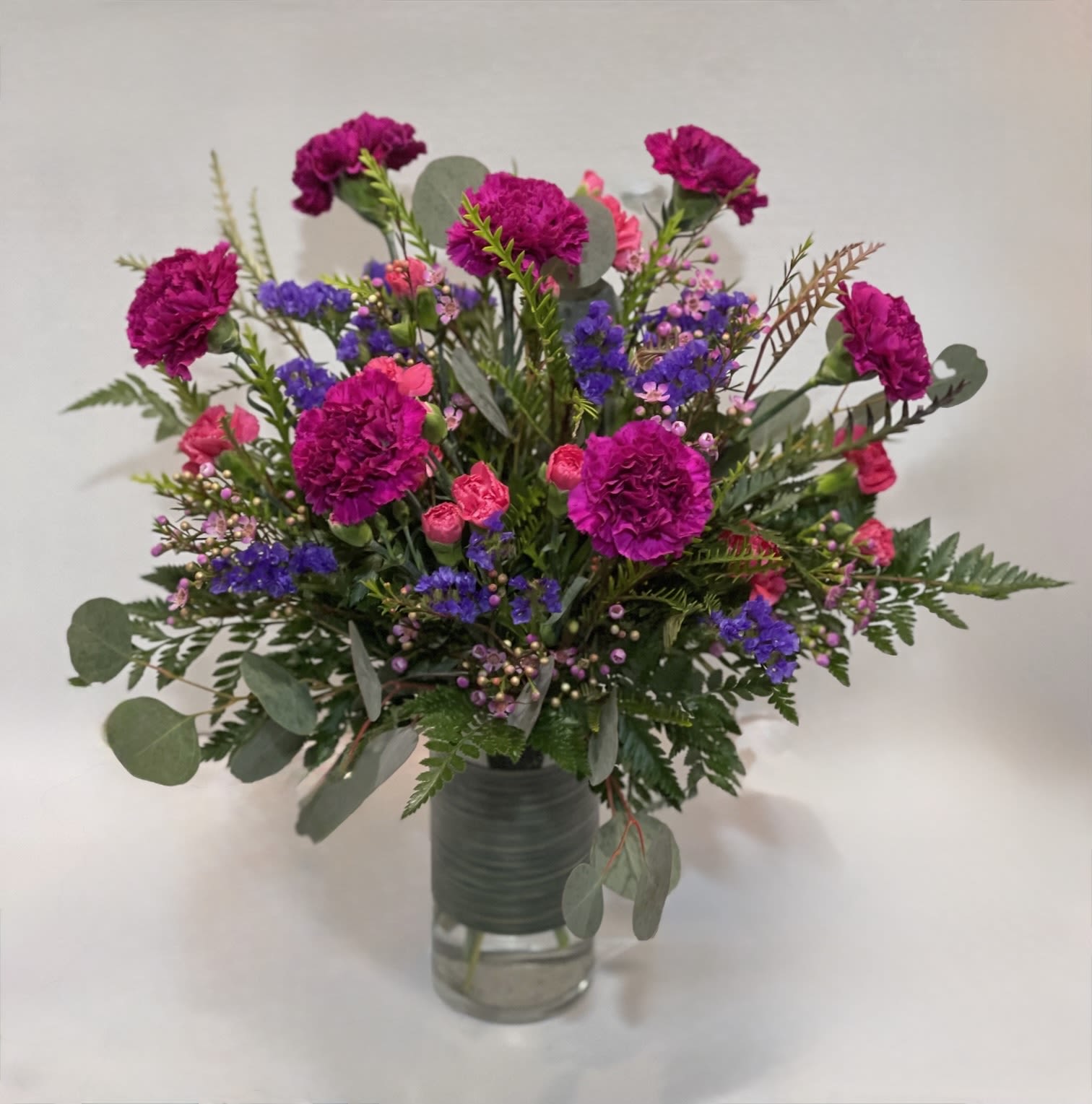 Bouquet of magenta carnations and purple filler flowers in a glass vase