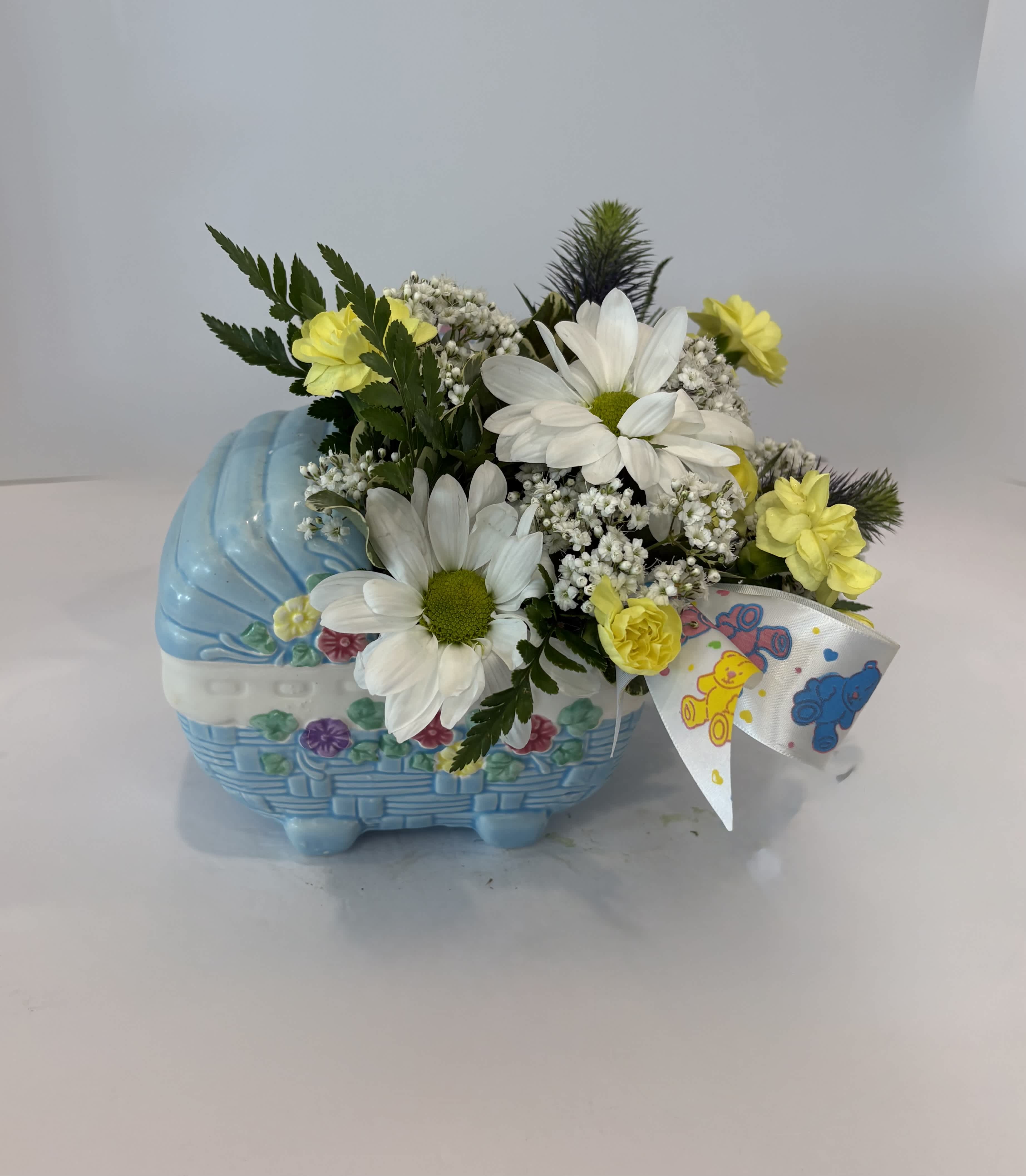 Yellow and white flowers arranged in a blue basket with a teddy bear ribbon