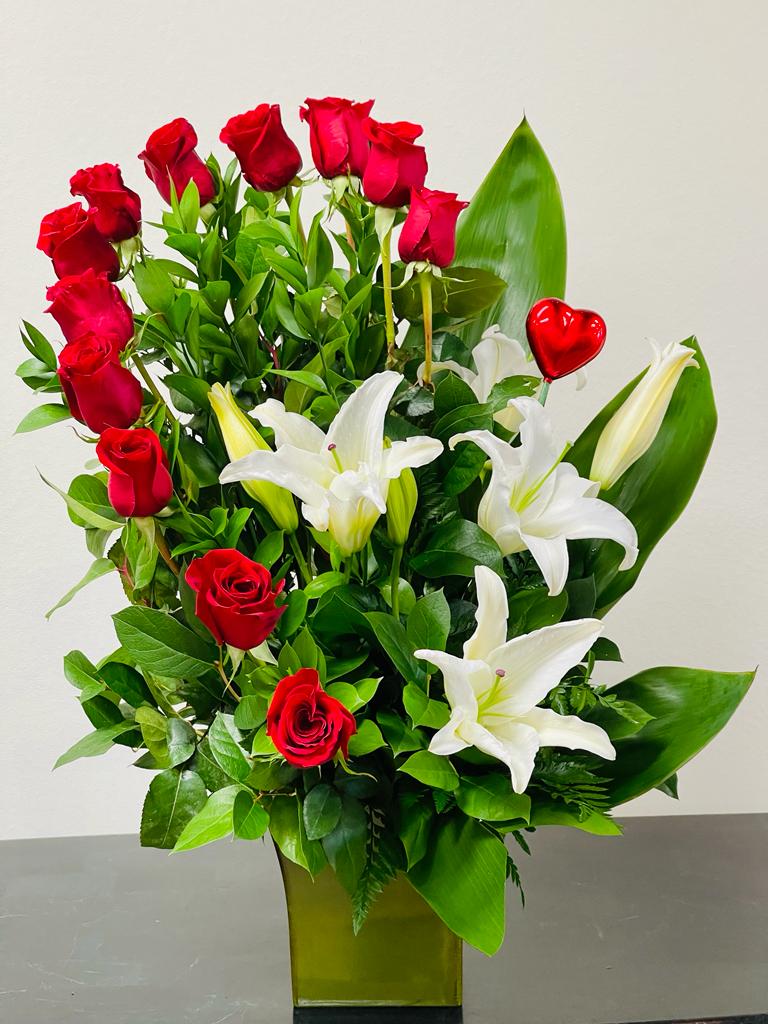 Red roses and white lilies in a tall green vase with a red heart pick