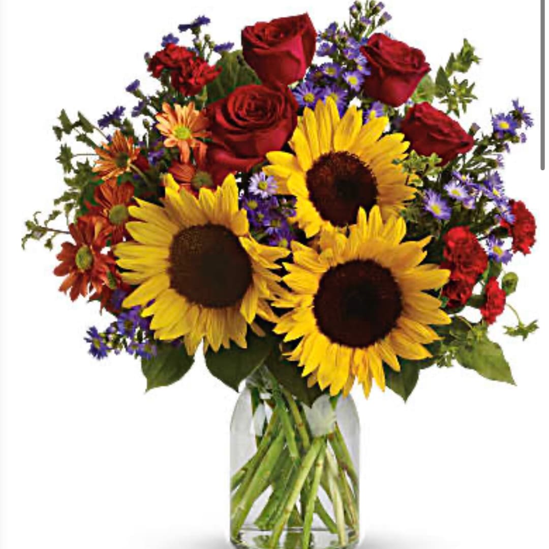 Bouquet of sunflowers, red roses, and purple flowers in a glass vase