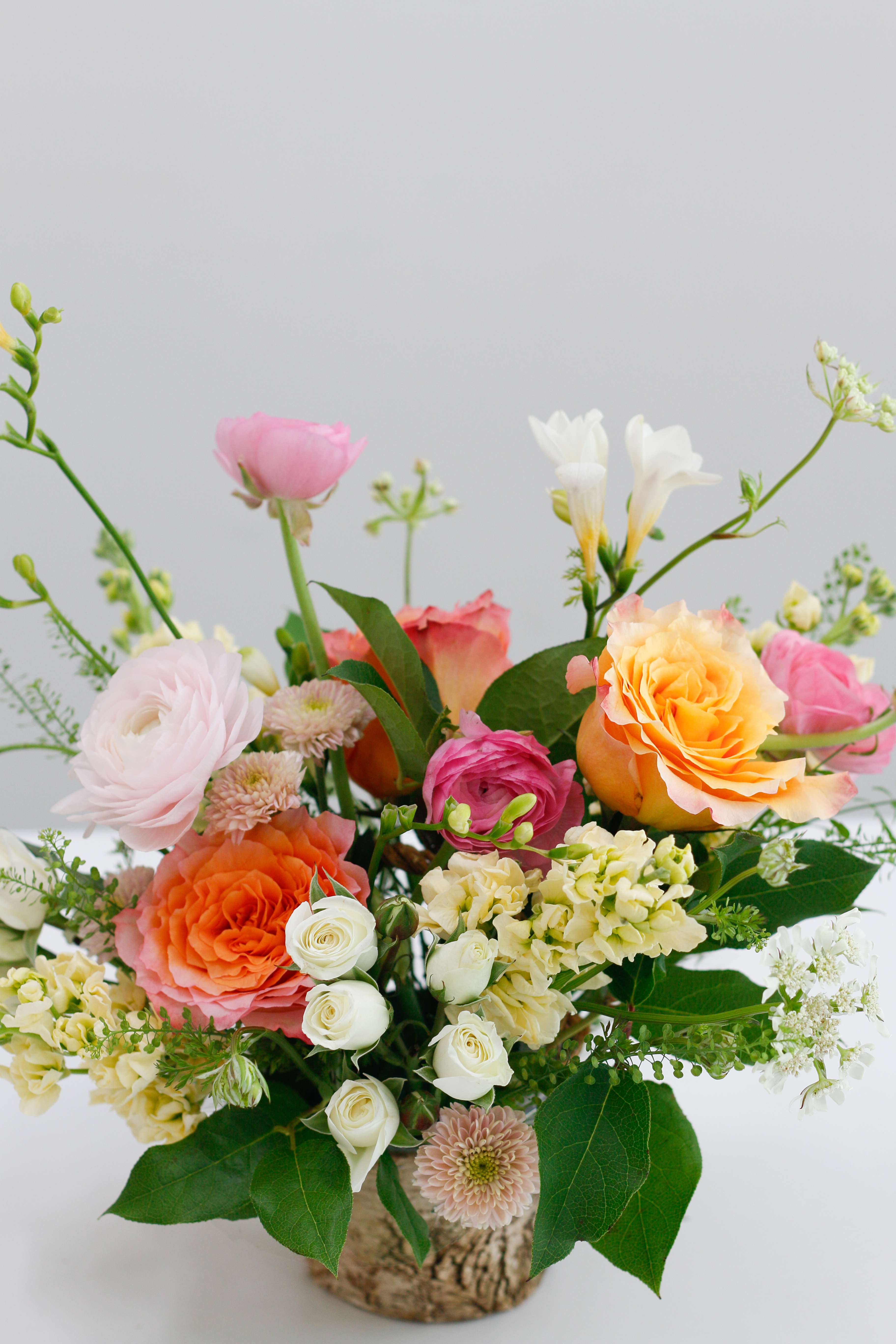 Mixed bouquet of roses, ranunculus, and white blooms in a rustic container