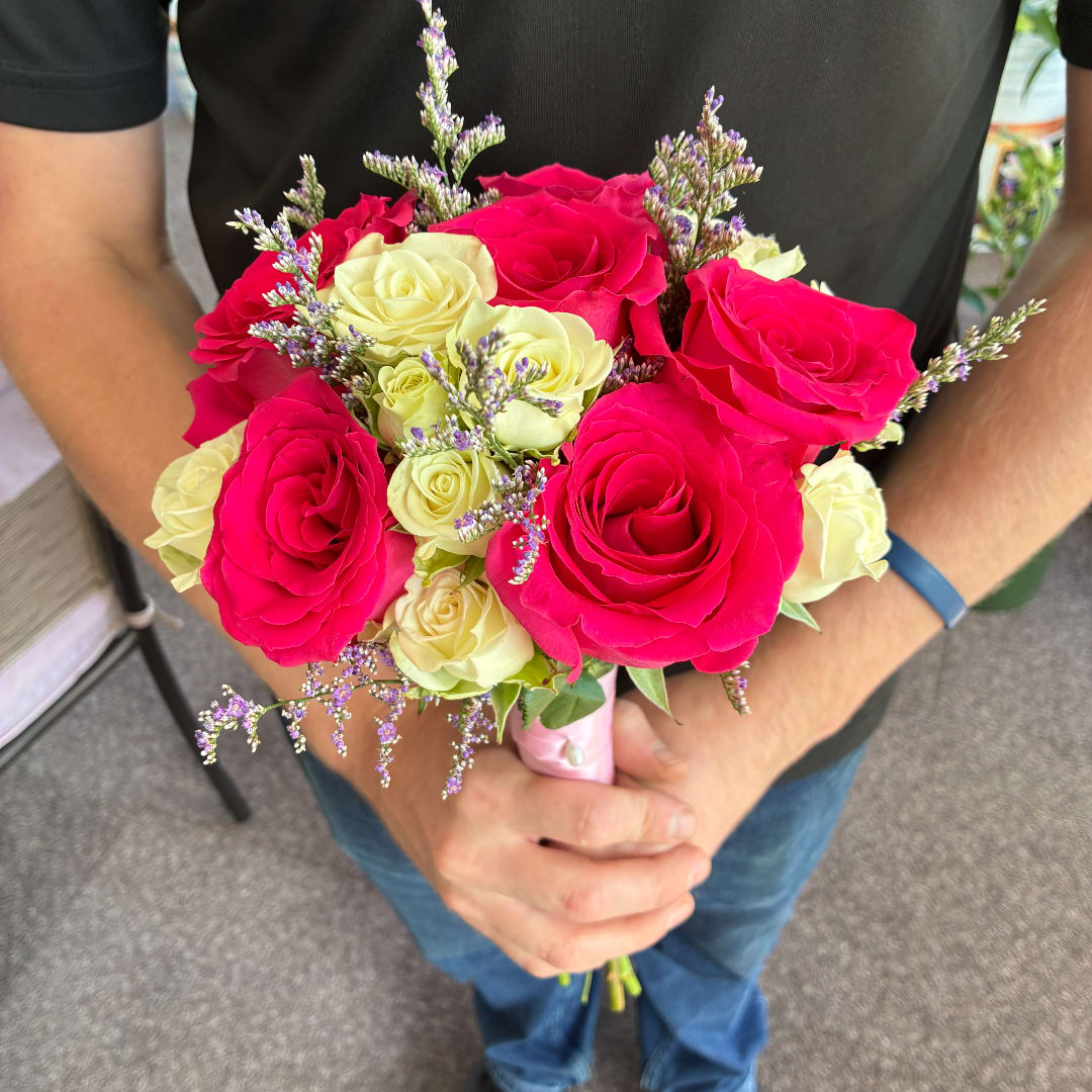 Handheld bouquet of pink and cream roses with small purple filler flowers