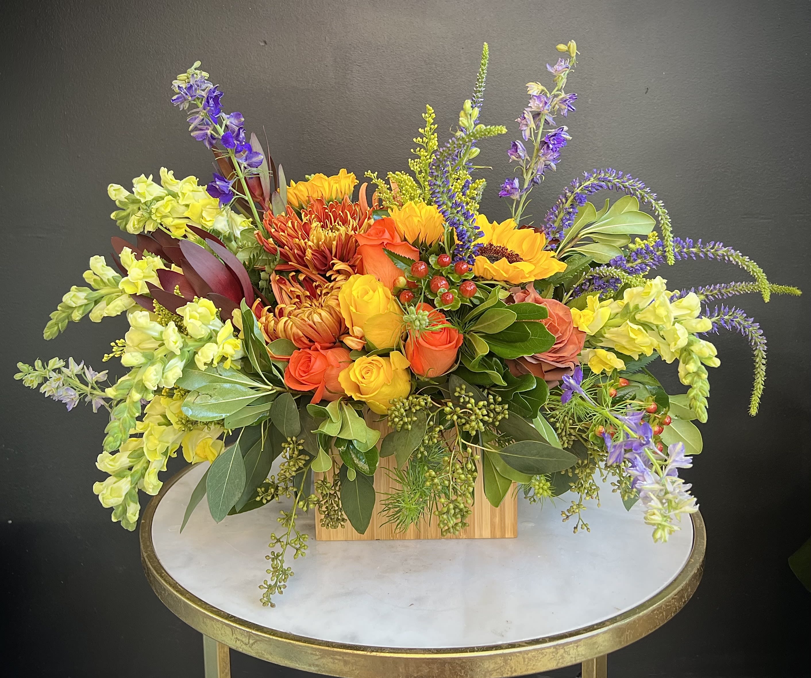 Colorful mixed flower arrangement in a wooden box on a round table