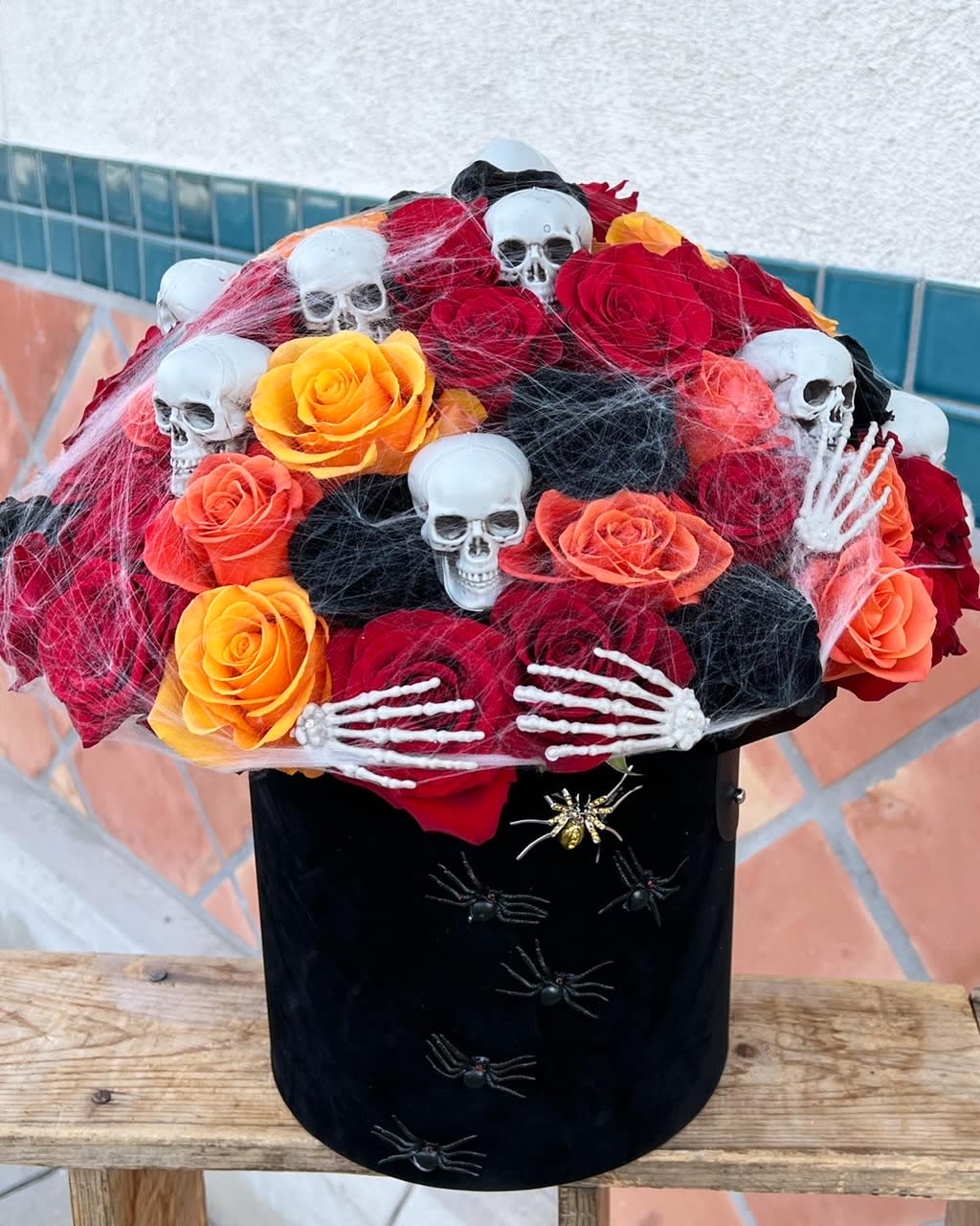 Velvet Midnight - Dare to decorate with darkness. This hauntingly beautiful Halloween bouquet features black, red, and orange roses elegantly arranged inside a luxurious black velvet flower box. Accented with a sinister skull, tangled spider webs, and creepy crawly spiders, Velvet Midnight brings a perfect mix of elegance and eerie charm — ideal for ghoulish gatherings or gothic gifts.