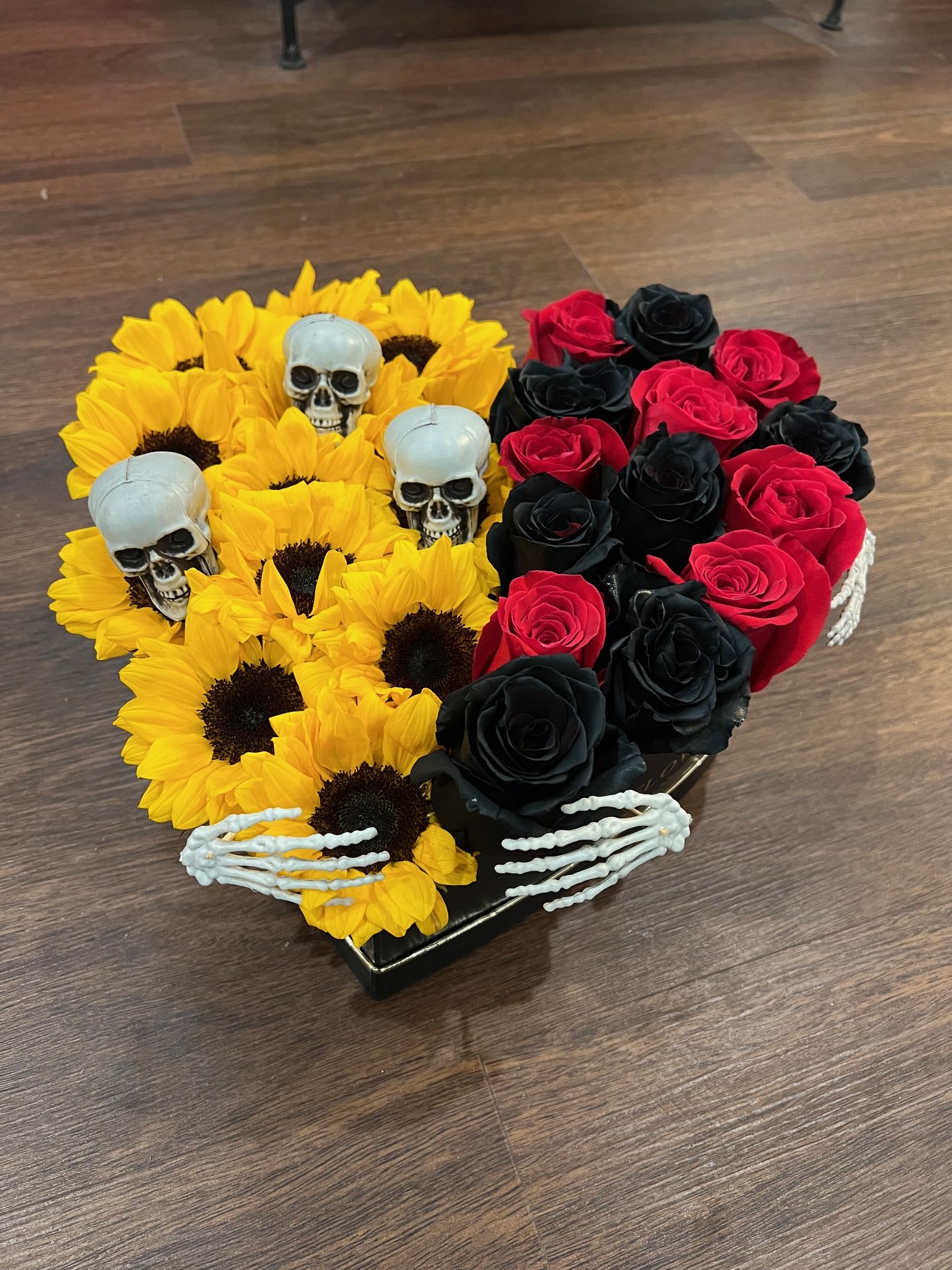 Spooktacular heart - sunflowers with red and black roses arranged inside a heart box with added skeleton.