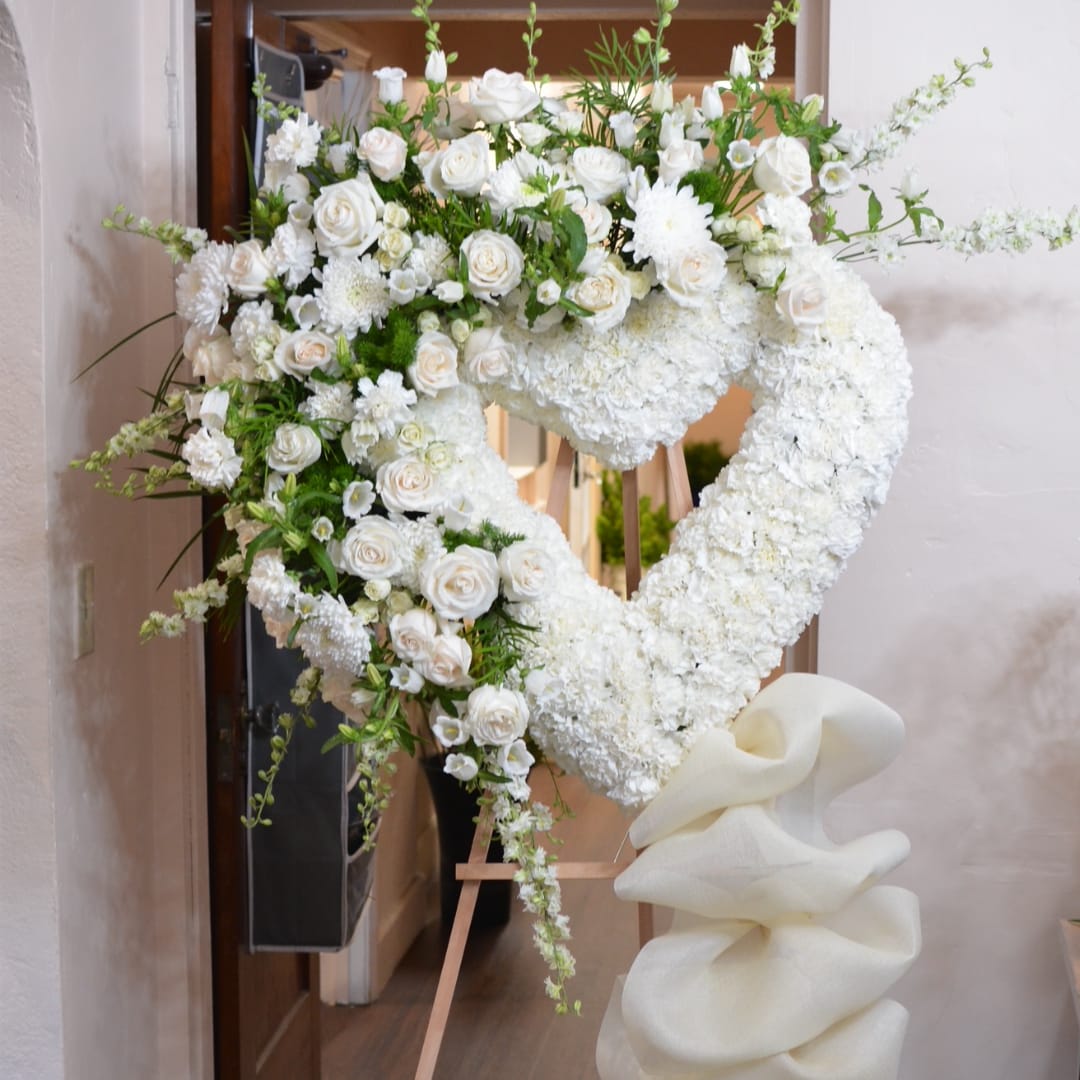 Heart-shaped white floral standing arrangement on an easel with a large white bow