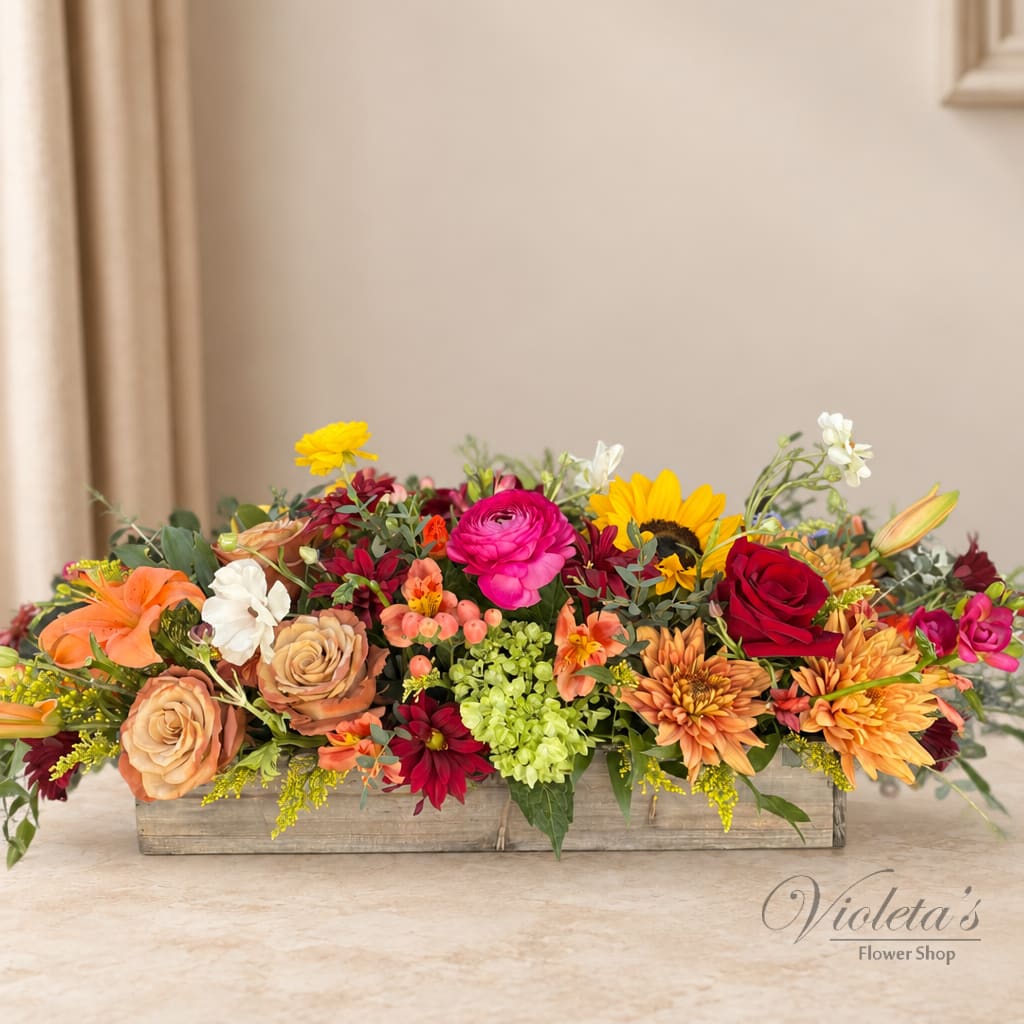 Low rectangular flower arrangement with roses, daisies, and sunflowers in a wooden box