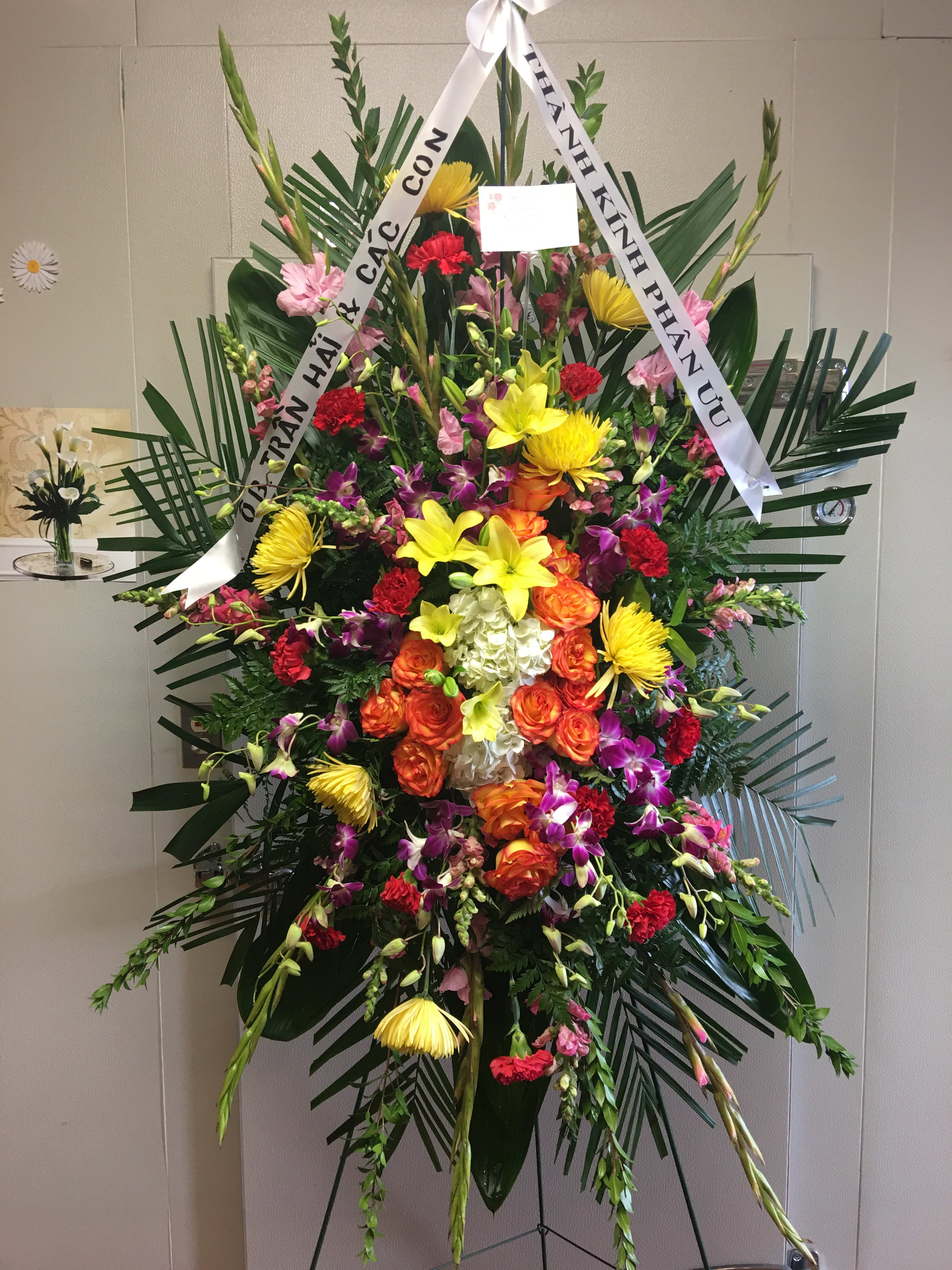 Large standing floral spray with colorful mixed blooms and white ribbons
