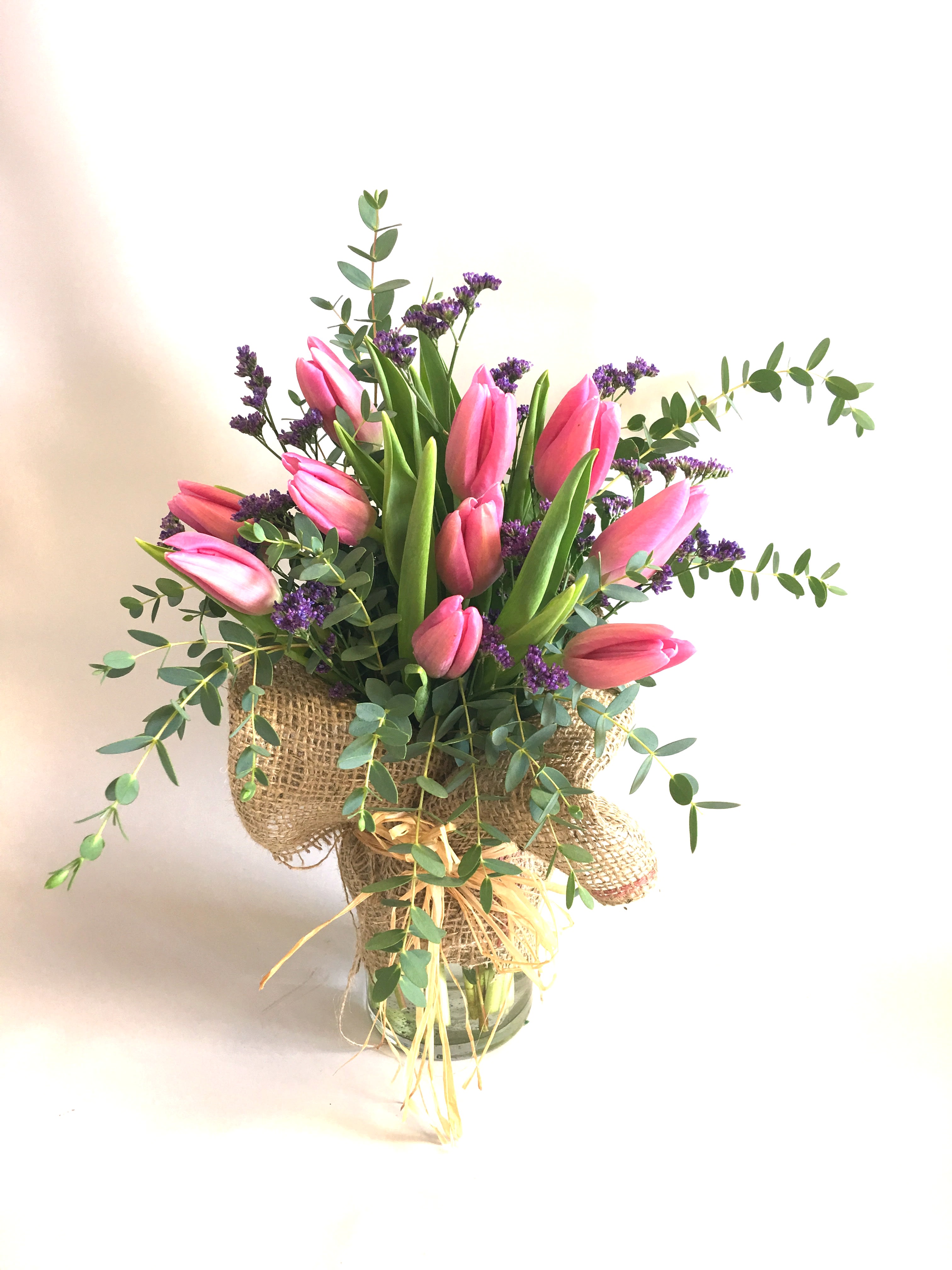 Pink tulips arranged in a burlap-wrapped vase with purple filler flowers