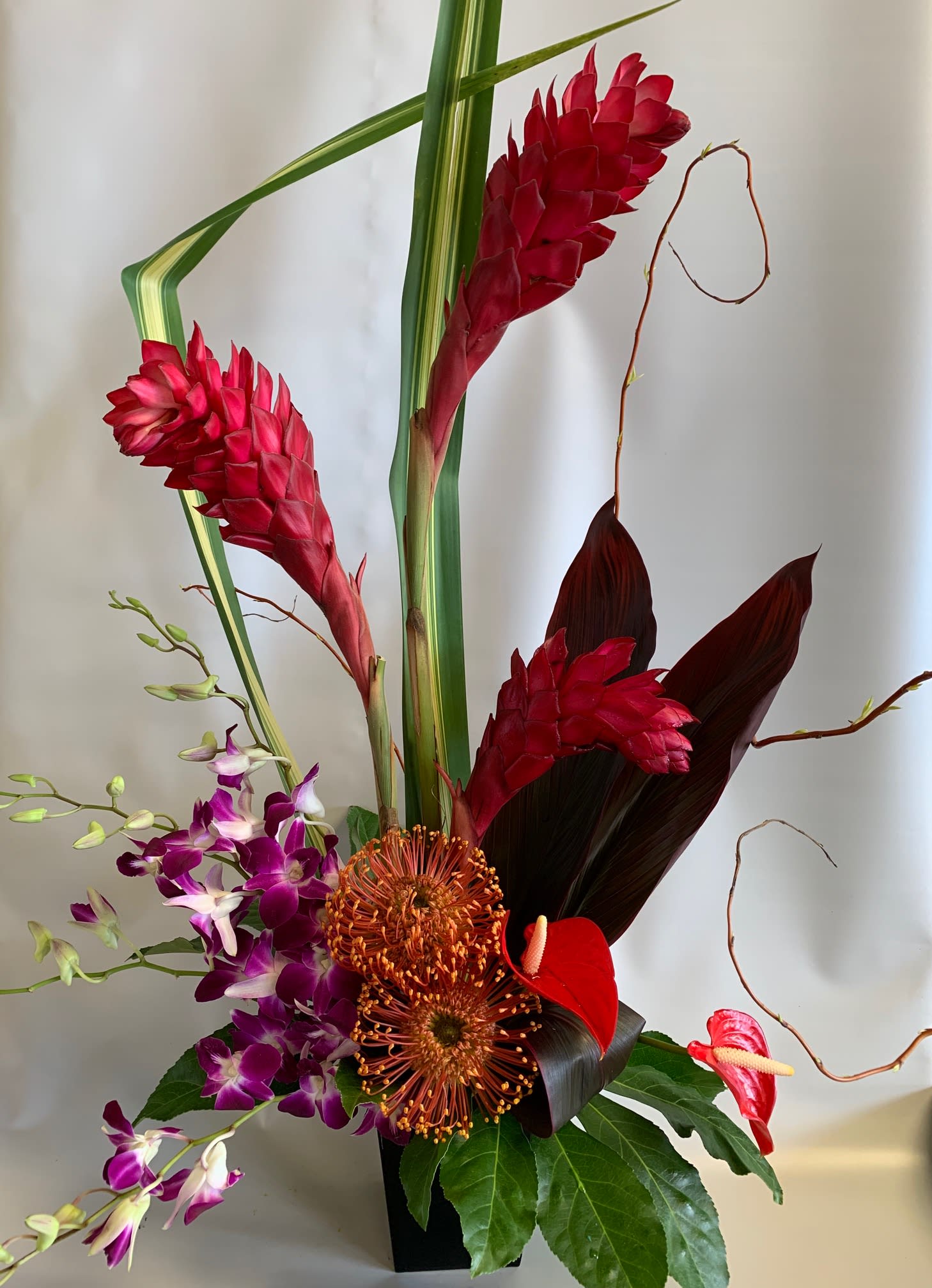 Tropical floral arrangement with red ginger, purple orchids, and anthuriums in a black vase