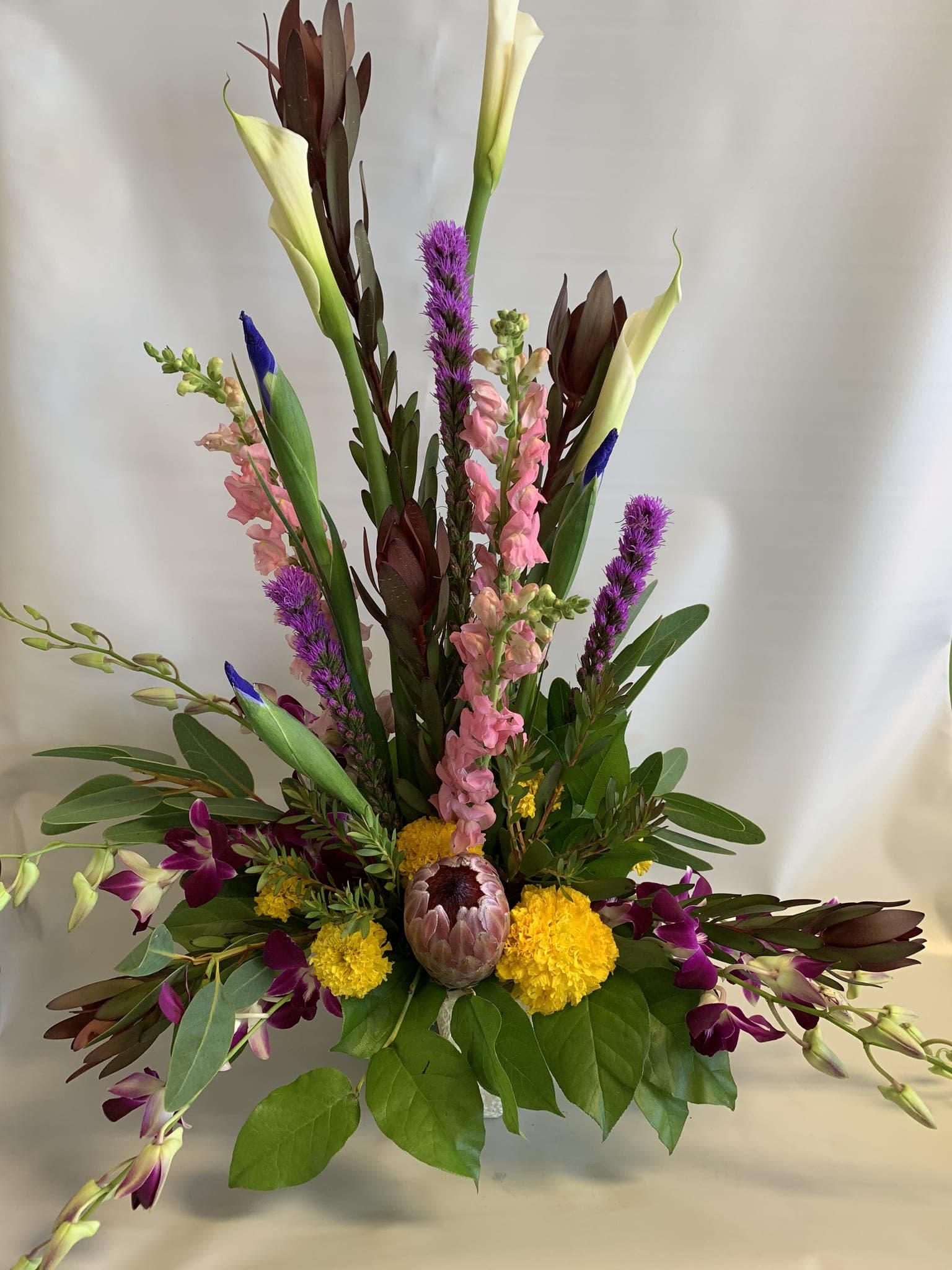 Tall mixed floral arrangement with calla lilies, orchids, and purple spikes