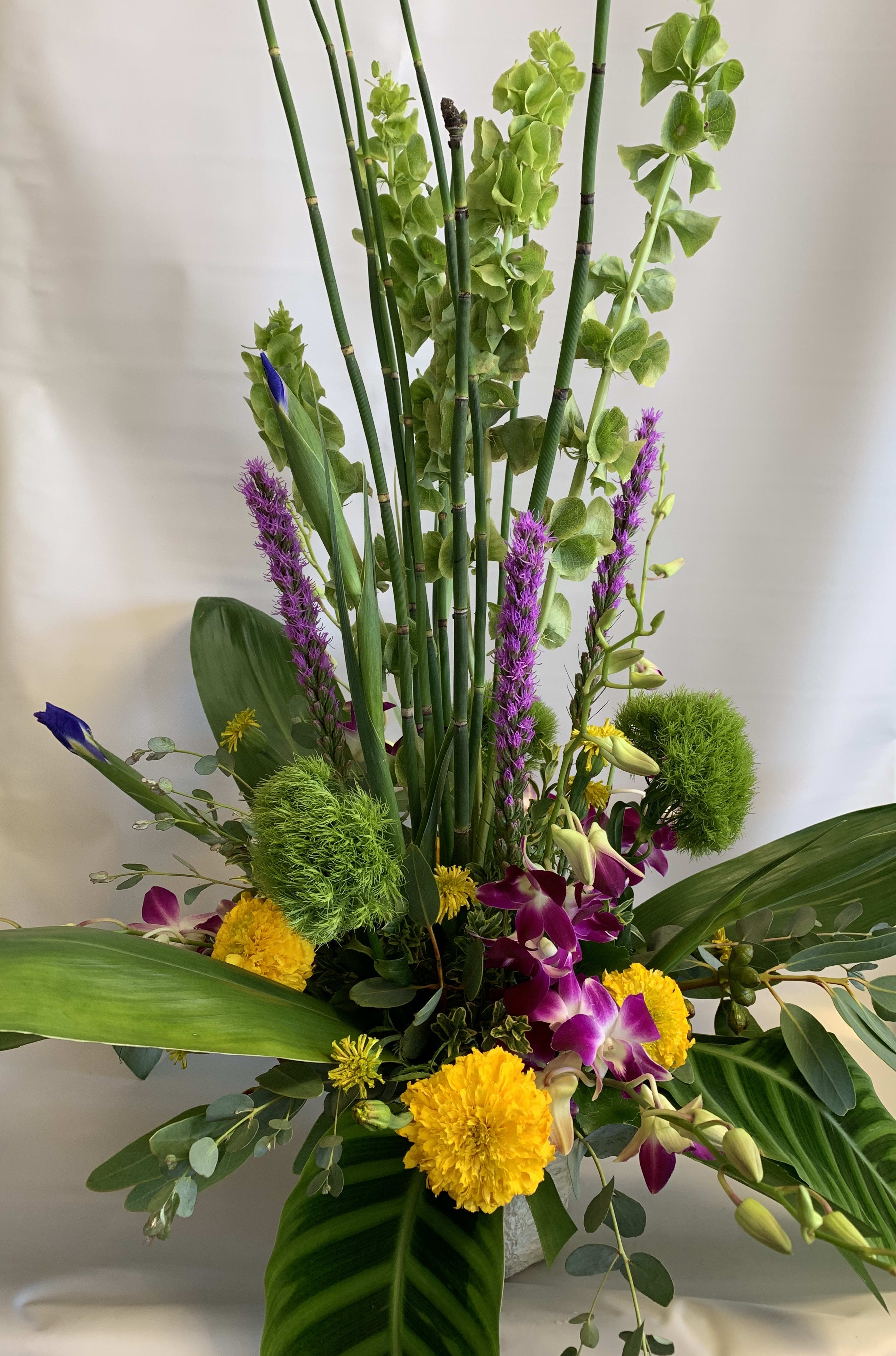 Tall tropical arrangement with purple orchids and yellow blooms in a vase