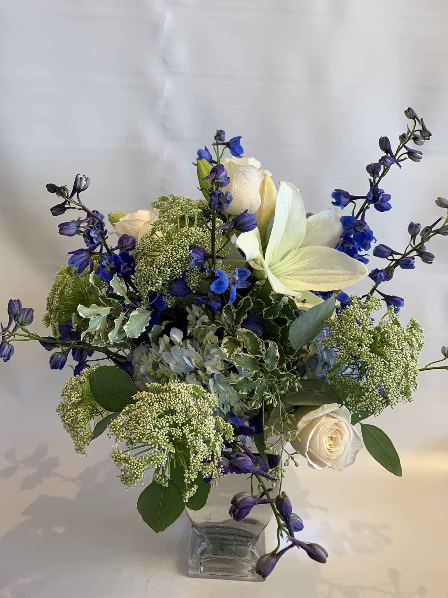 White roses and blue flowers in a clear glass vase
