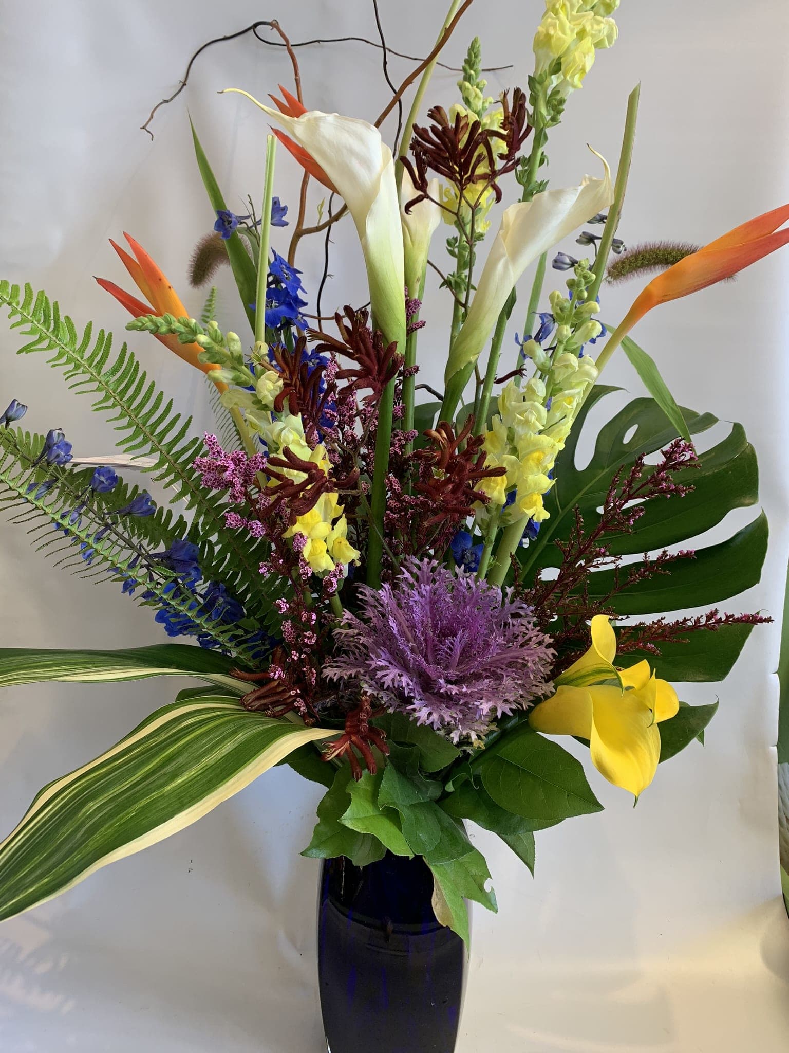 Tall tropical bouquet with calla lilies, orchids, and bird-of-paradise in a dark vase
