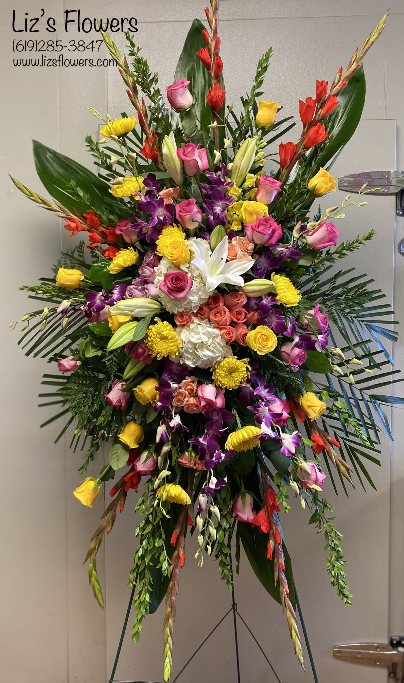 Large standing floral spray with roses, lilies, orchids, and yellow blooms