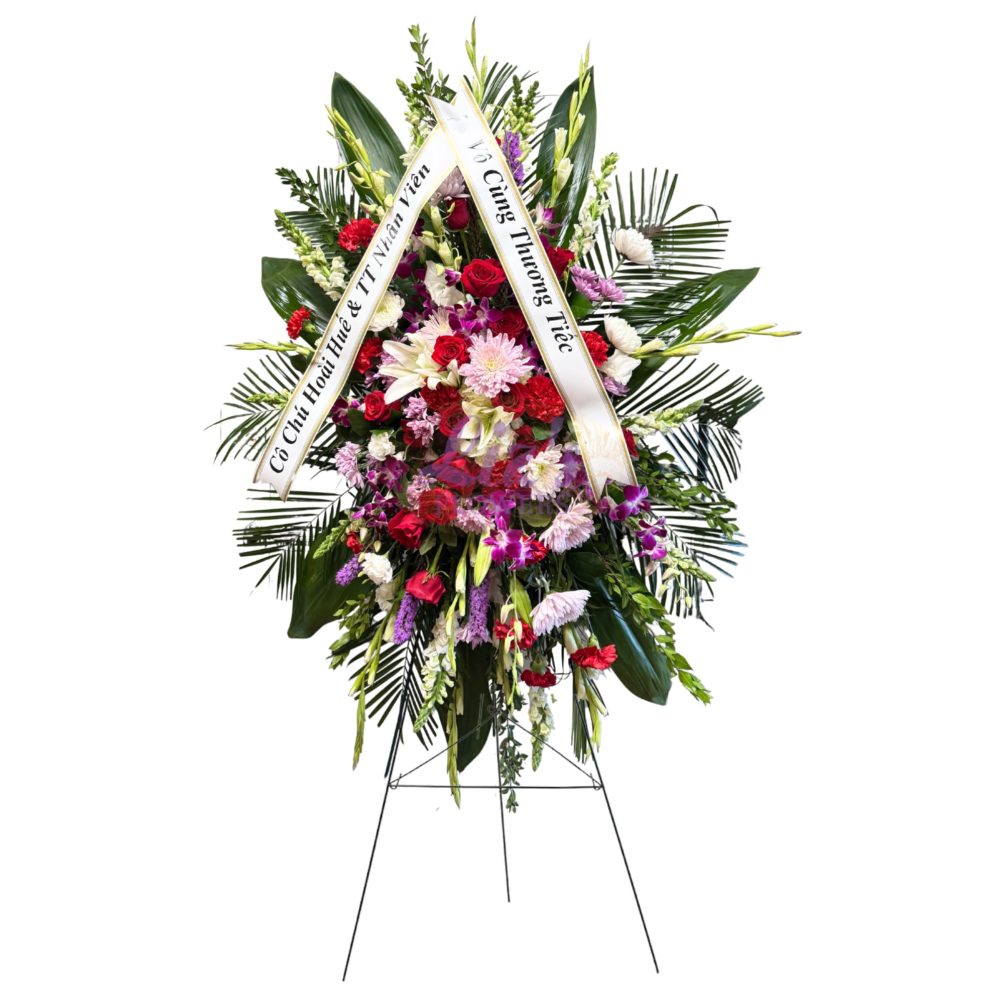 Tall standing sympathy spray with red roses, white lilies, and purple blooms on an easel.