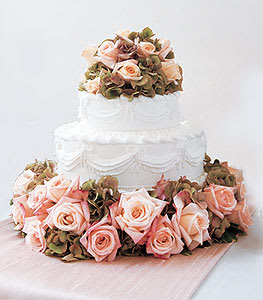 White tiered cake surrounded by pale pink roses