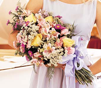 Woman holding a mixed bouquet of pink and yellow flowers with a lavender ribbon