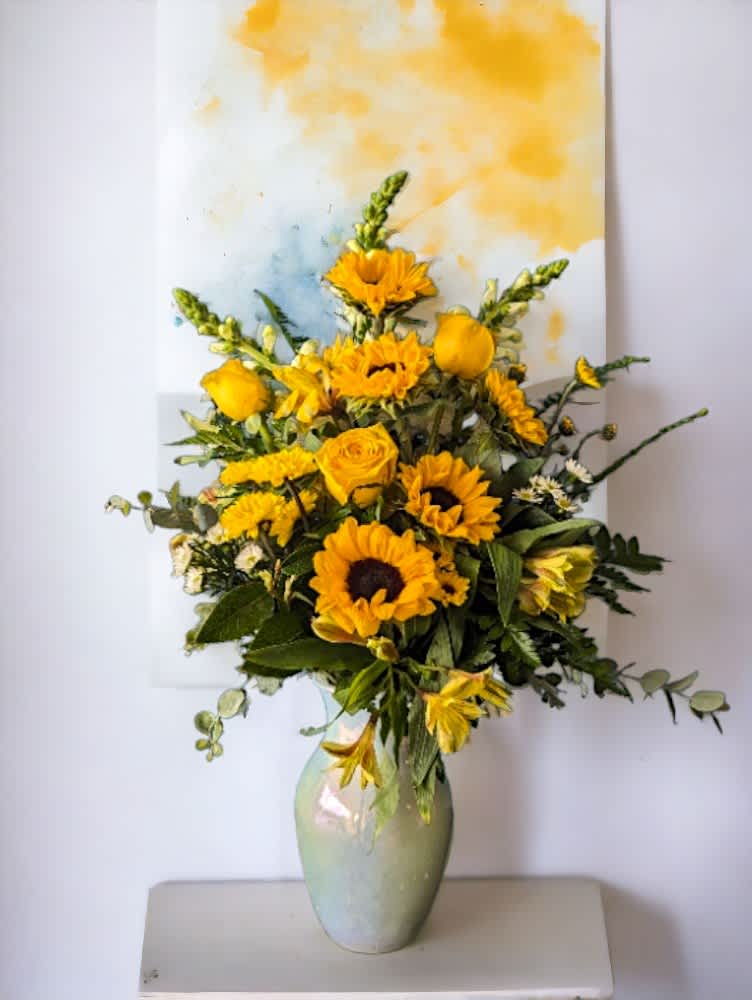 "Sunlight" from the Rainbow Collection by Art &amp; Flowers - Introducing "Sunlight" from the Rainbow Collection by Art &amp; Flowers—a brilliant all-yellow one sided floral arrangement that radiates happiness, optimism, and warmth. This cheerful masterpiece features a delightful mix of sunflowers, roses, daisies and more, meticulously arranged to capture the essence of a sunny day. Perfect for brightening any occasion, "Sunlight" brings a burst of joy and positivity, making it the ideal choice for celebrations, congratulations, or simply to uplift someone's spirits. Let the vibrant hues and joyful design of "Sunlight" illuminate your space with its radiant charm.  Flower varieties may vary slightly, but arrangement will be styled true to the picture with all yellow flowers filled to value. 
